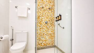 Une salle de bain comprenant des toilettes, une douche avec un mur recouvert de mosaïques et une porte de douche en verre.