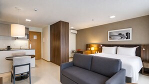 A hotel room with a bed, a sofa, a desk with a chair, a small table, and a wall-mounted picture.