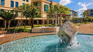 A hotel with a clear blue sky, a fountain, and a pool.