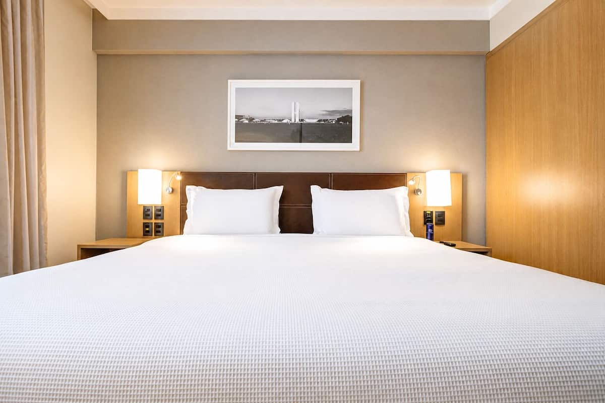 A hotel room with a large bed, two bedside tables, a headboard, and a framed picture on the wall.