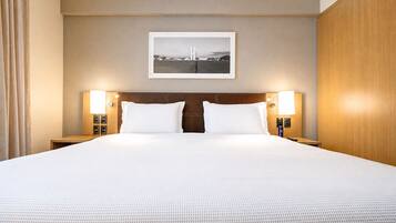 Una habitación de hotel con una cama grande, dos mesitas de noche, un cabecero y un cuadro enmarcado en la pared.