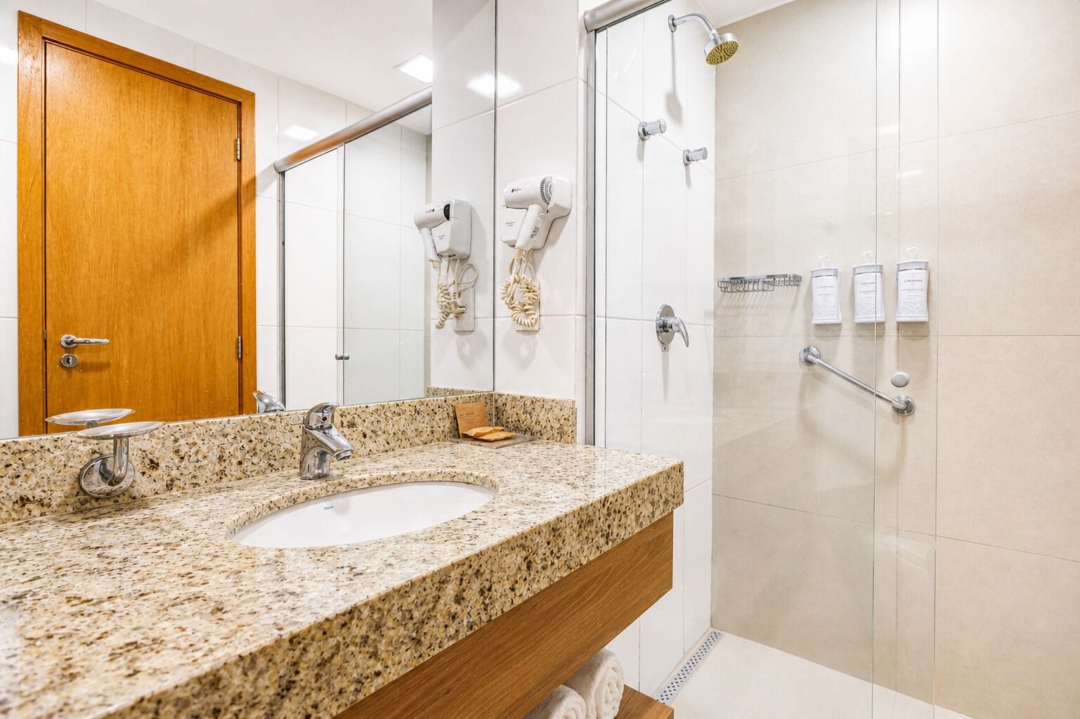 A bathroom with a granite countertop sink, a wooden door, and a glass shower enclosure.