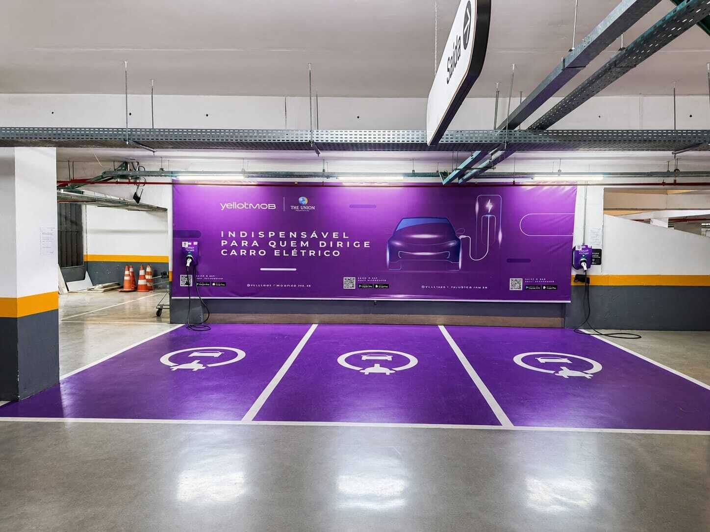 A parking area with electric car charging stations, a purple floor, and a sign for yellowlotmob.