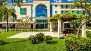 A hotel with a large arched entrance, a signboard, and a well-maintained garden with benches and pathways.