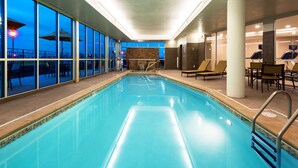 Una piscina interior con paredes de vidrio transparente, sillones de descanso y vistas al cielo nocturno.