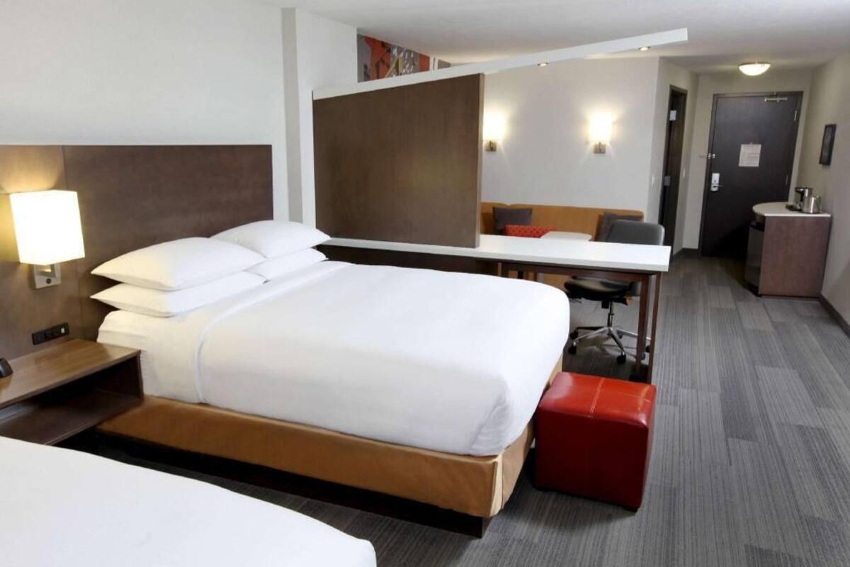 A hotel room with a bed, desk, chair, and a small kitchenette.