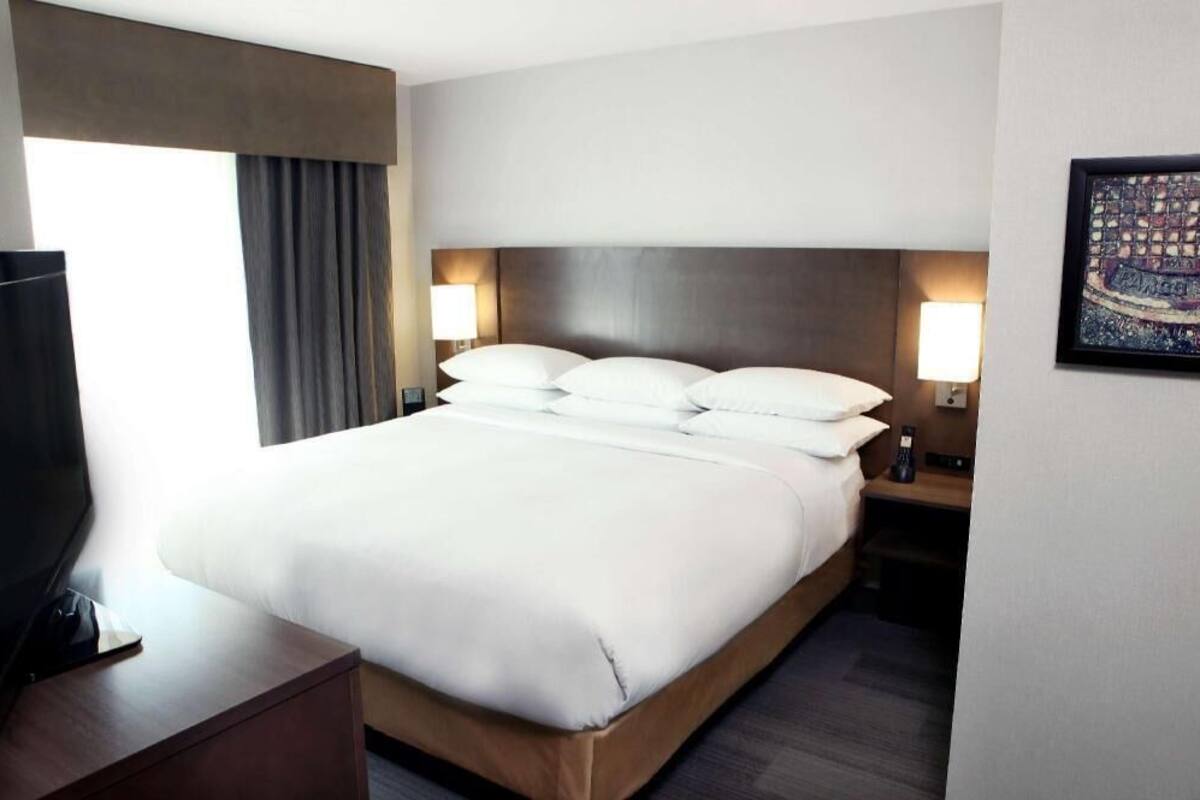 A hotel room with a large bed, bedside lamps, a TV on a wooden side table, and a window with curtains.