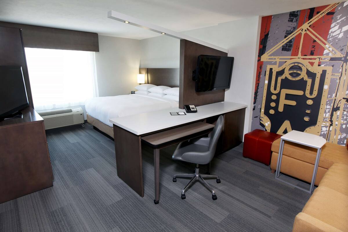 A hotel room with a bed, desk, chair, TV, and a large window.