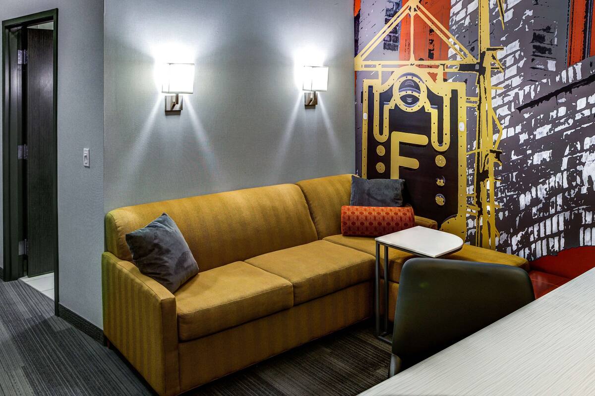 A modern hotel room with a sofa, a small table, and a decorative wall piece.