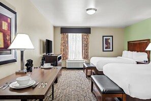 A hotel room with a bed, a desk with a lamp, a television, and a window with curtains.