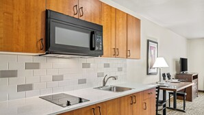 A modern kitchen with wooden cabinets, a built-in microwave, a sink, and a dining area with a table and chairs. - Ledgestone Suites Hotel Billings (Billings)
