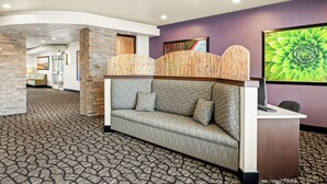 A reception area with a sofa, desk, and a large green floral artwork on the wall. - Ledgestone Suites Hotel Billings (Billings)