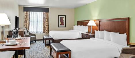 Une chambre d’hôtel avec deux lits, un bureau avec une chaise, une petite table, une lampe et une fenêtre avec des rideaux.
