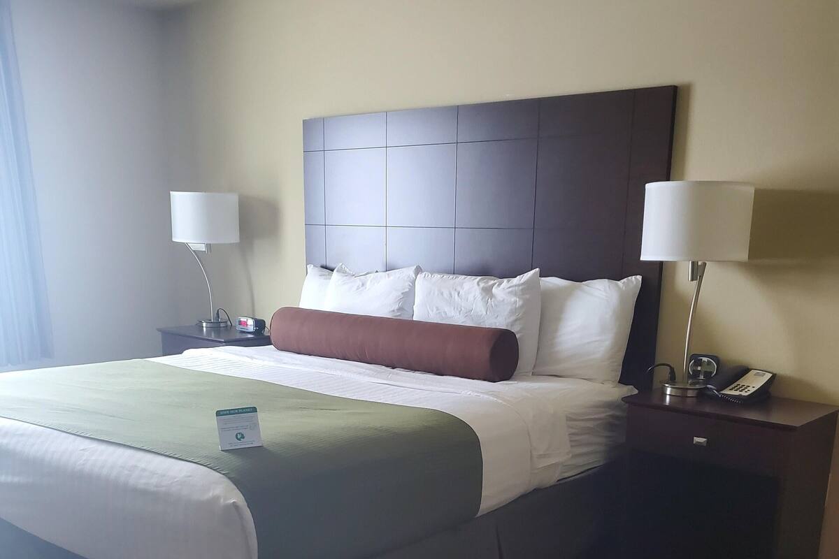 Habitación de hotel con una cama grande, dos mesitas de noche y una lámpara a cada lado.