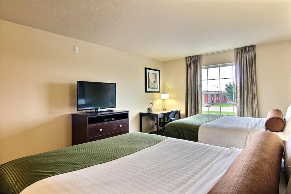 Habitación de hotel con dos camas, televisión, escritorio con silla y ventana con cortinas.