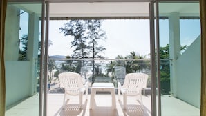 A balcony with a glass door, two white plastic chairs, and a small table. - Time Out Hotel Beach Front (Patong)