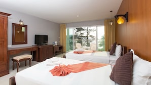 A hotel room with two beds, a desk with a television, a chair, and a large window with a view of trees. - Time Out Hotel Beach Front (Patong)