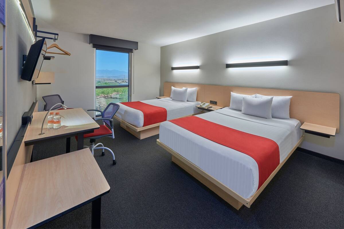 A hotel room with two beds, a desk, a chair, a TV, and a window with a view.