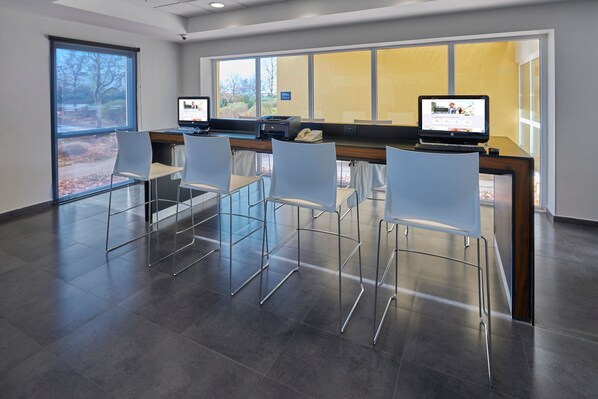 Una zona de recepción moderna con un mostrador, dos monitores de computadora y cuatro sillas blancas.
