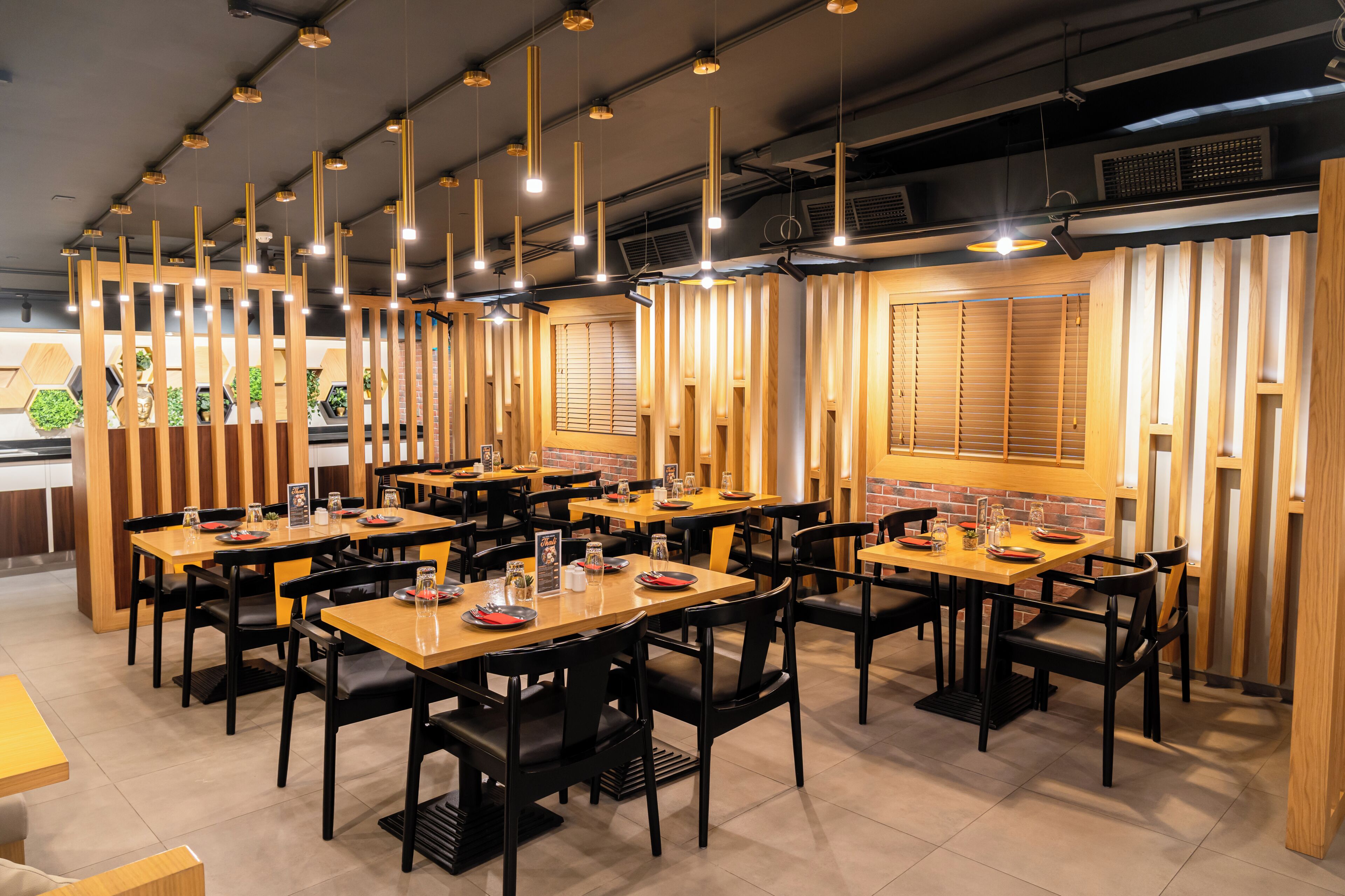 Un restaurante con varias mesas y sillas, separadores de madera y lámparas colgantes.