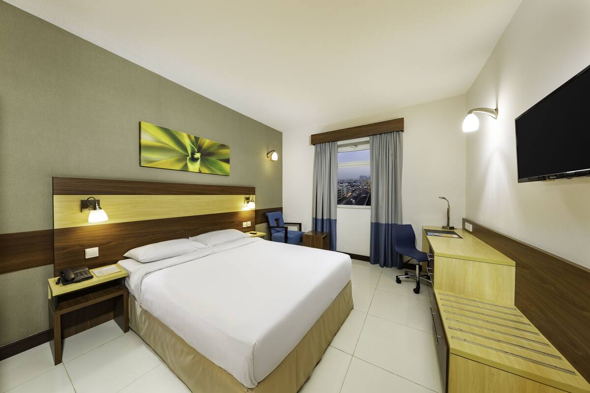 Een hotelkamer met een bed, bureau, stoel en uitzicht op de stad door het raam.