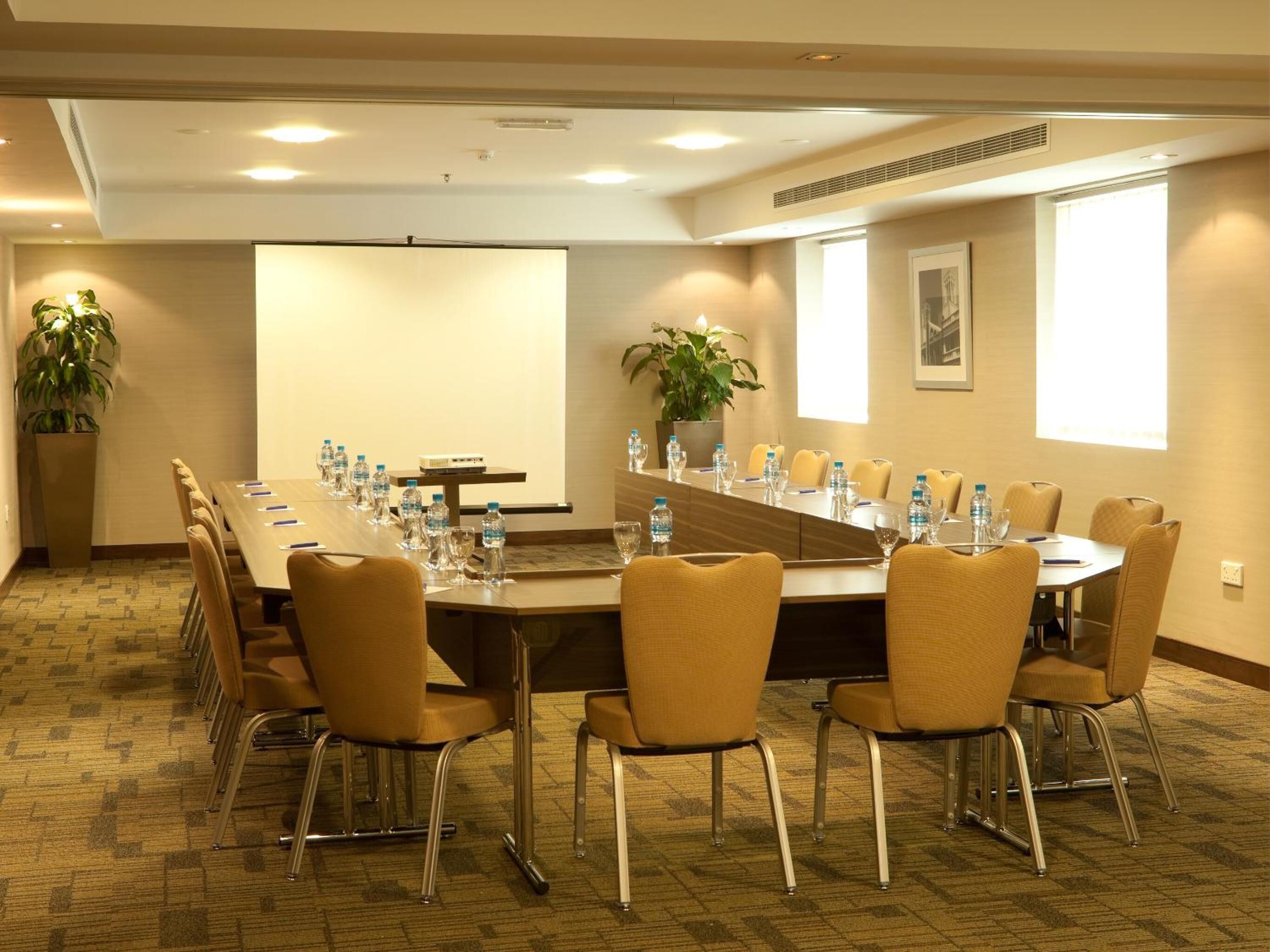 A conference room with a long table, chairs, water bottles, and a projector screen.