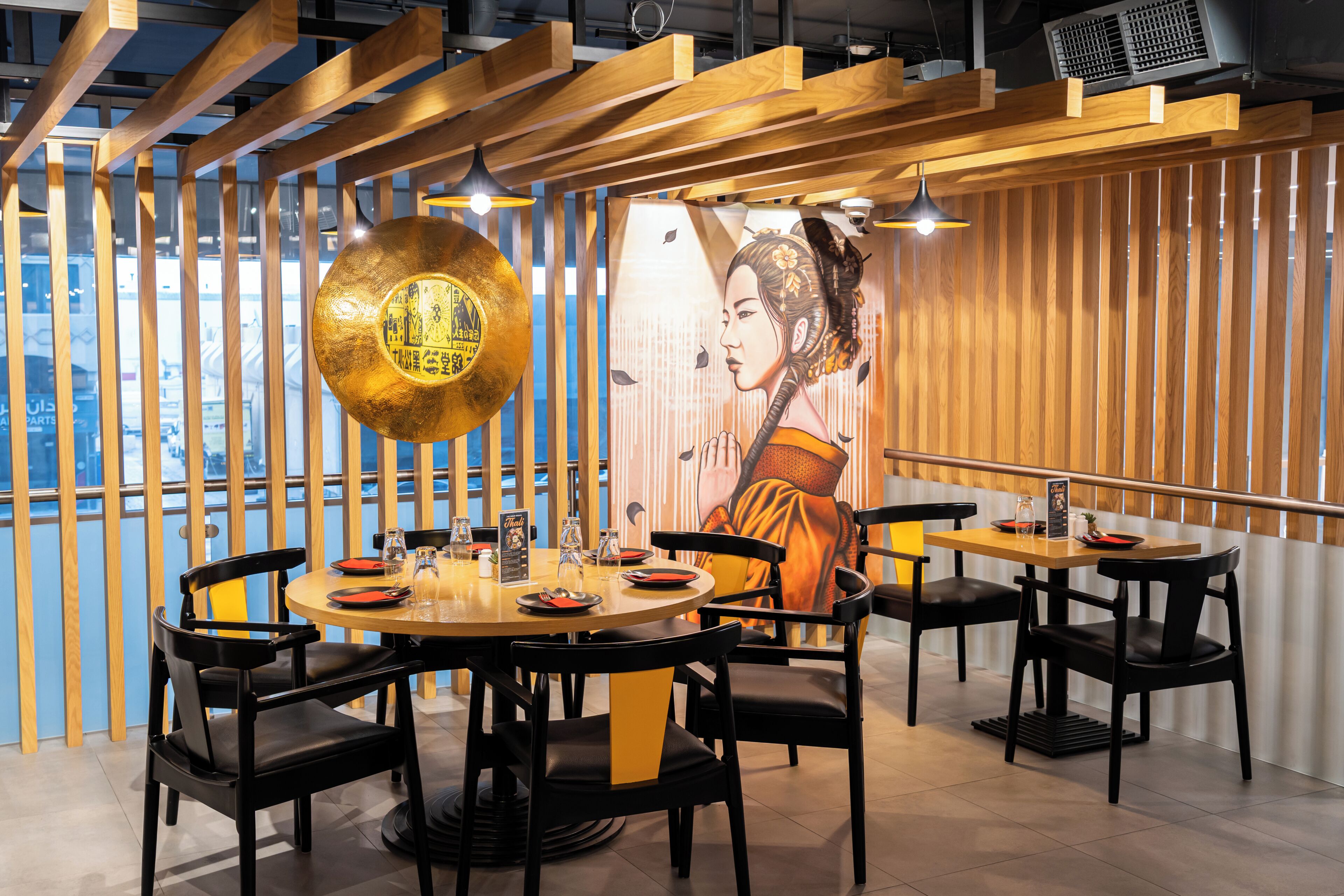 A restaurant interior with round tables, black chairs, wooden beams, and a mural on the wall.