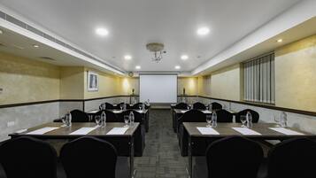 A conference room with long tables, chairs, water bottles, and a projector screen.