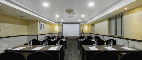 A conference room with long tables, chairs, water bottles, and a projector screen.