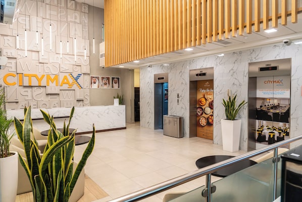 A hotel lobby with a reception desk, elevators, a dining area, and a staircase.