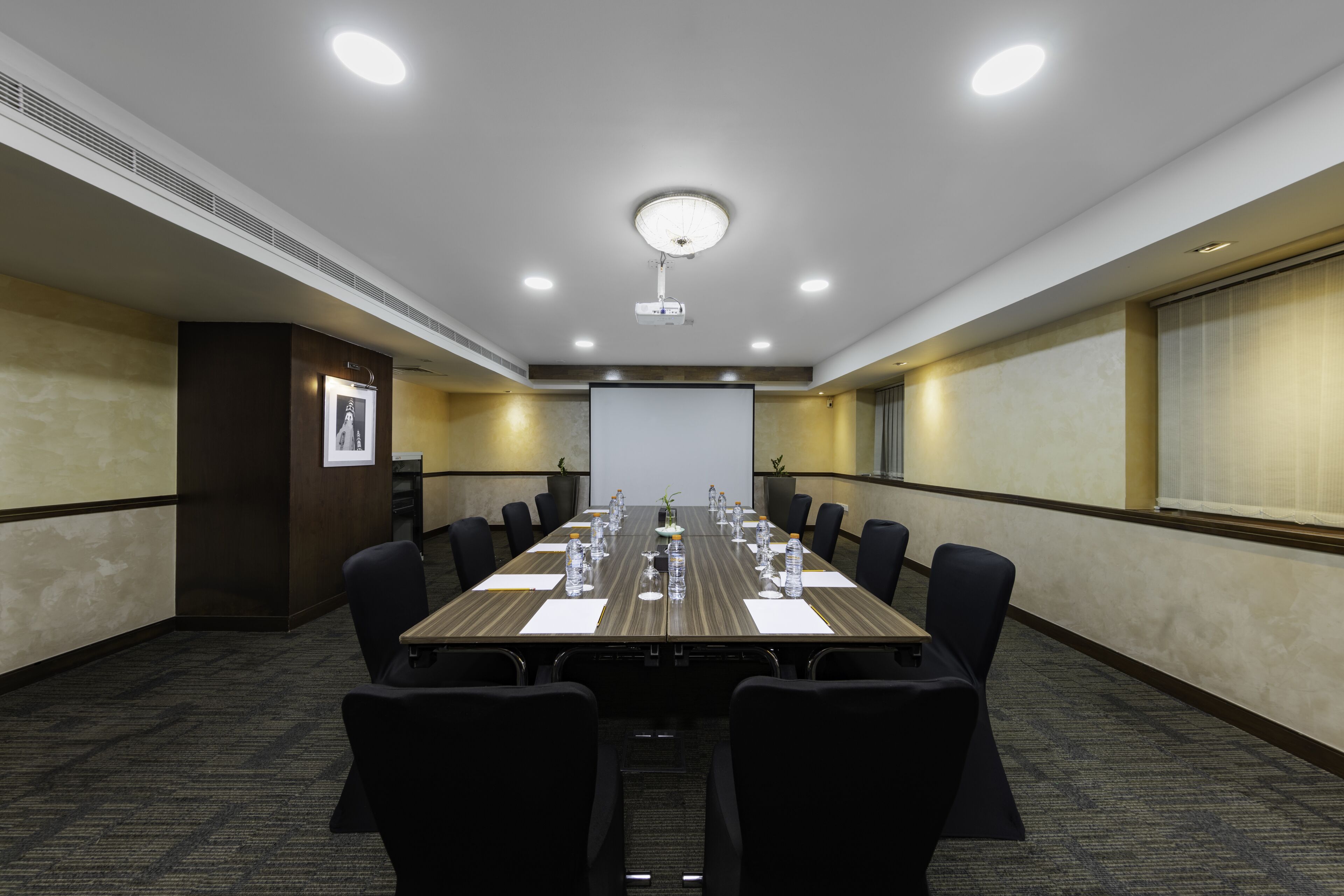 A conference room with a long table, black chairs, and a projector screen.