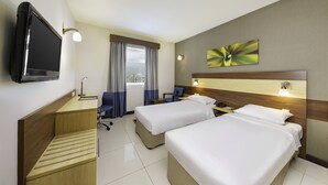 Une chambre d’hôtel avec deux lits, un bureau, une télévision et une fenêtre avec des rideaux.