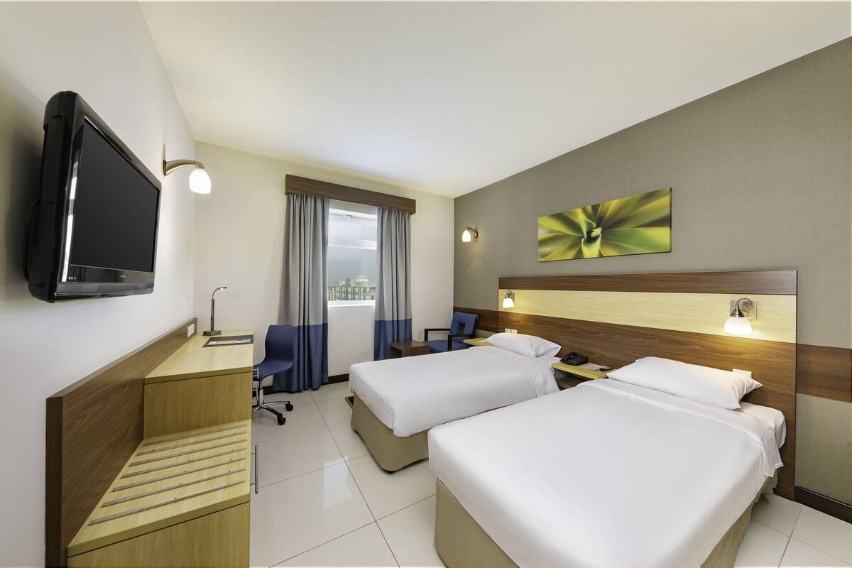 Een hotelkamer met twee bedden, een bureau, een televisie en een raam met gordijnen.