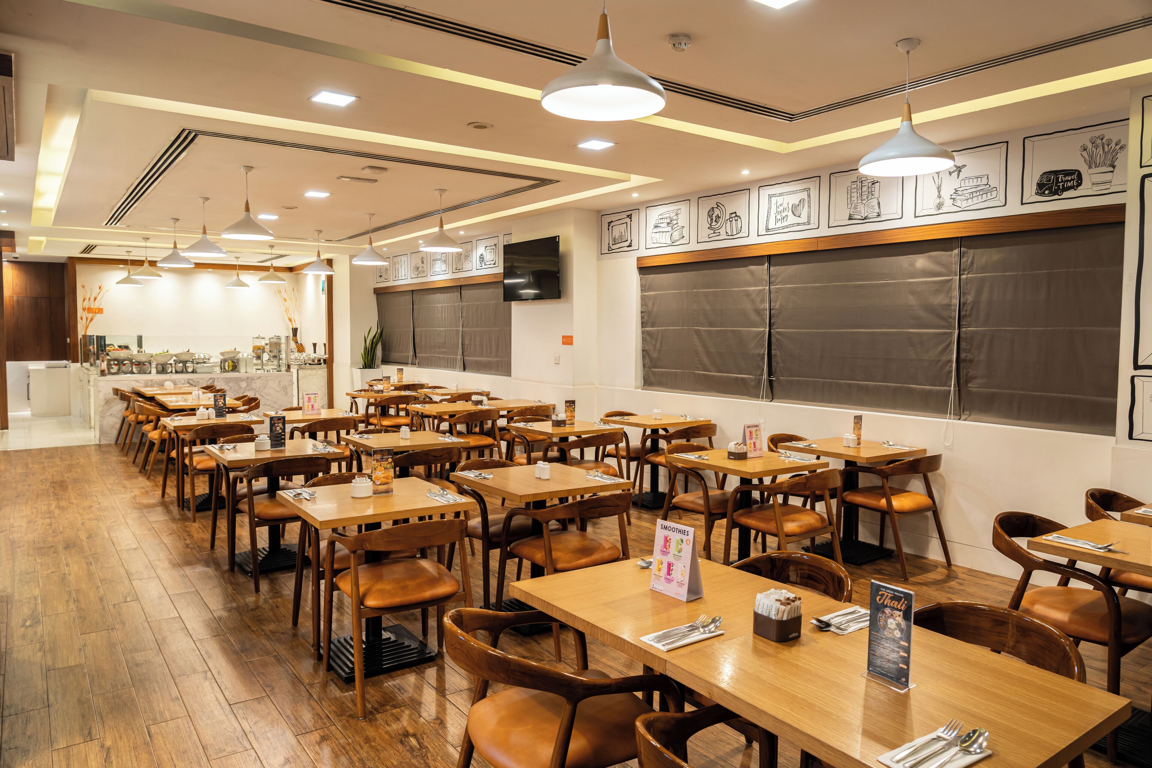Un interno ristorante con tavoli e sedie in legno, illuminazione a sospensione, opere d'arte incorniciate alle pareti e un'ampia finestra.