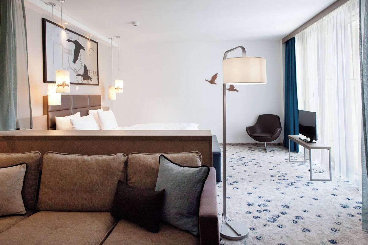 Una habitación de hotel con sofá, cama, televisor, lámpara y un cuadro en la pared.