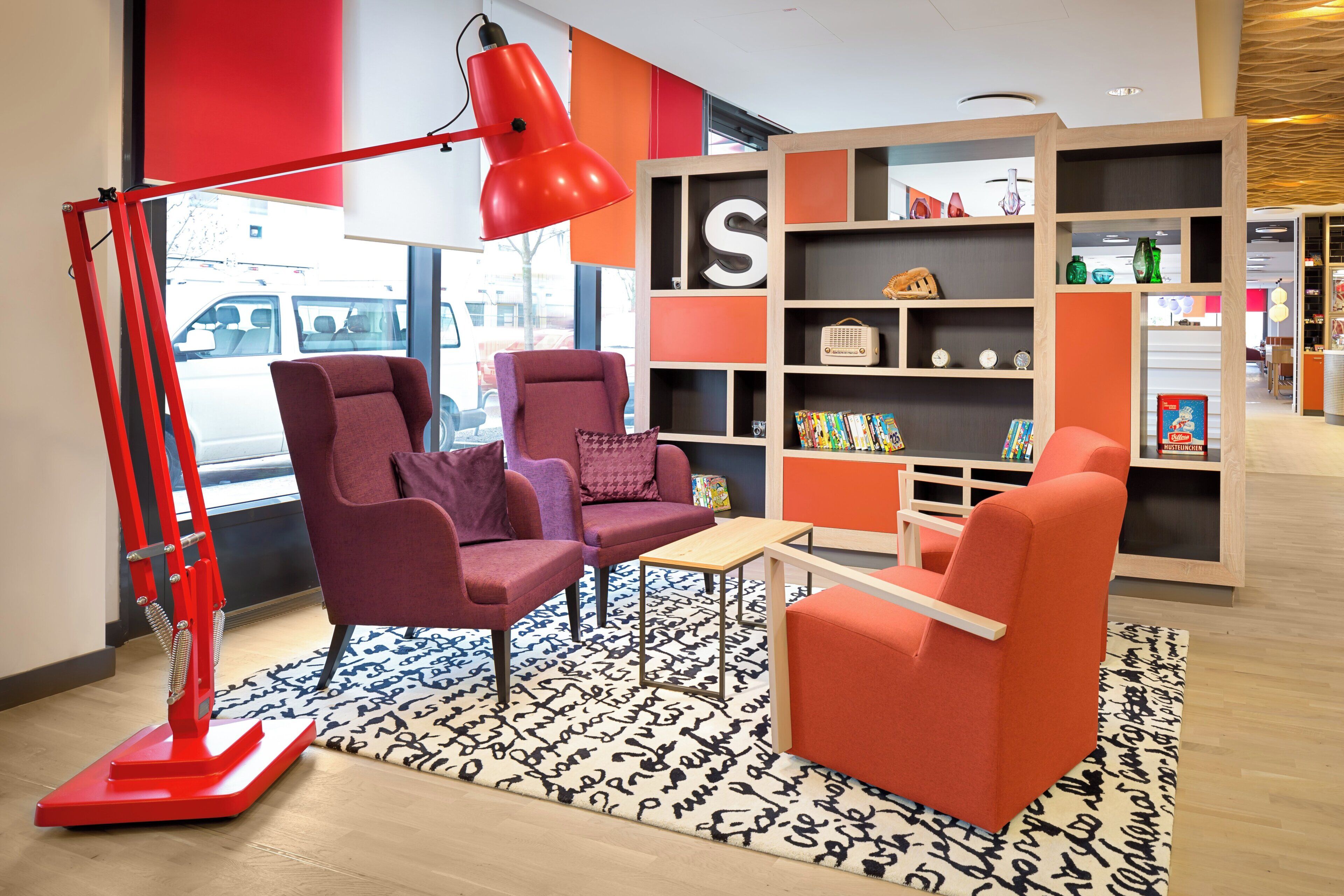 Un interior moderno con dos sillones, una lámpara de pie roja y una estantería con diversos objetos.