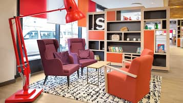 Un interior moderno con dos sillones, una lámpara de pie roja y una estantería con diversos objetos.