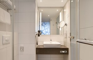 A modern bathroom with a white sink, a towel rack, a hairdryer, and a mirror. - Holiday Inn Berlin - City East Side by IHG (Berlin)
