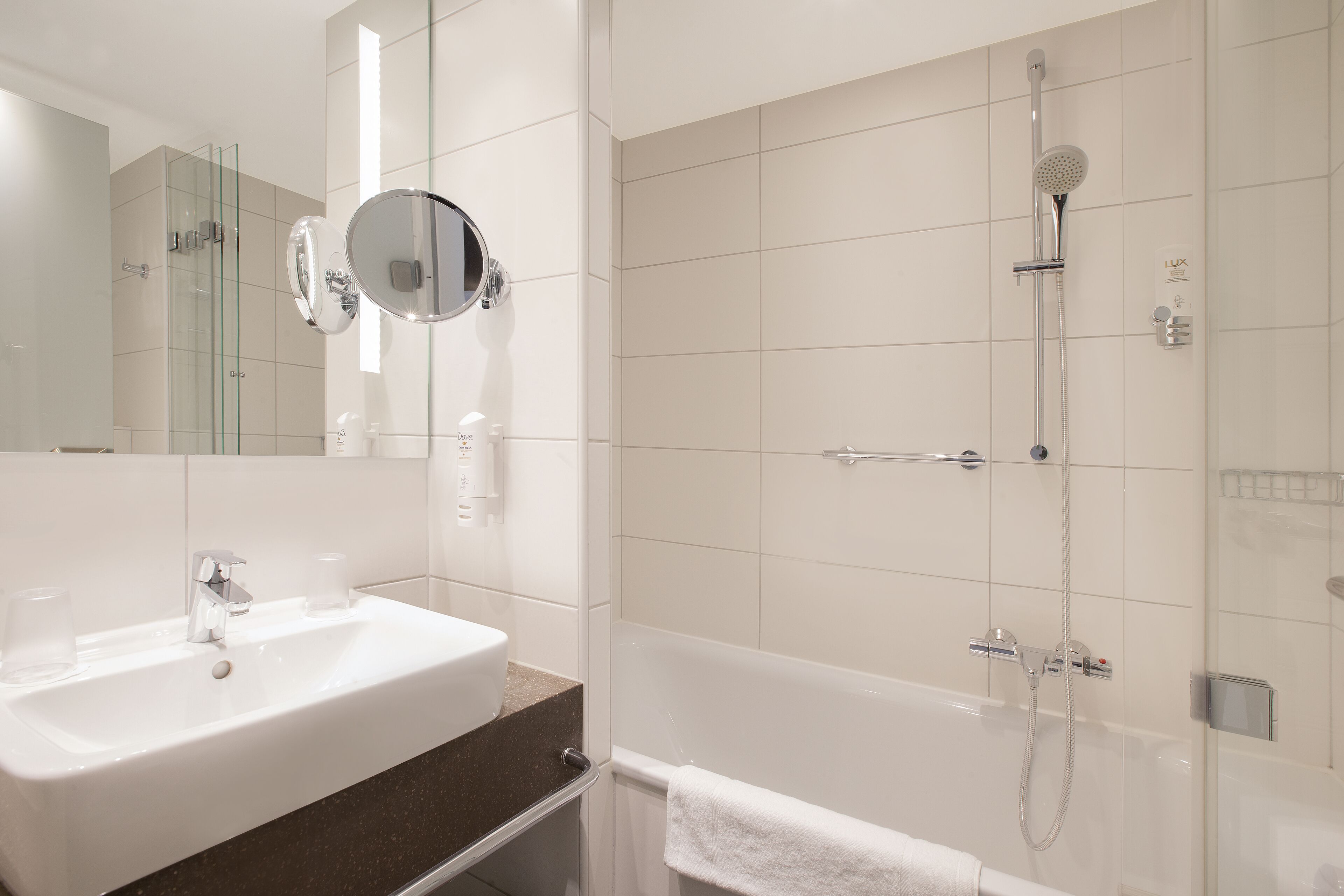 A modern bathroom with a white sink, a round mirror, a glass-enclosed shower, and a white towel hanging on the wall.