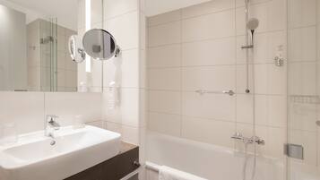 A modern bathroom with a white sink, a round mirror, a glass-enclosed shower, and a white towel hanging on the wall.