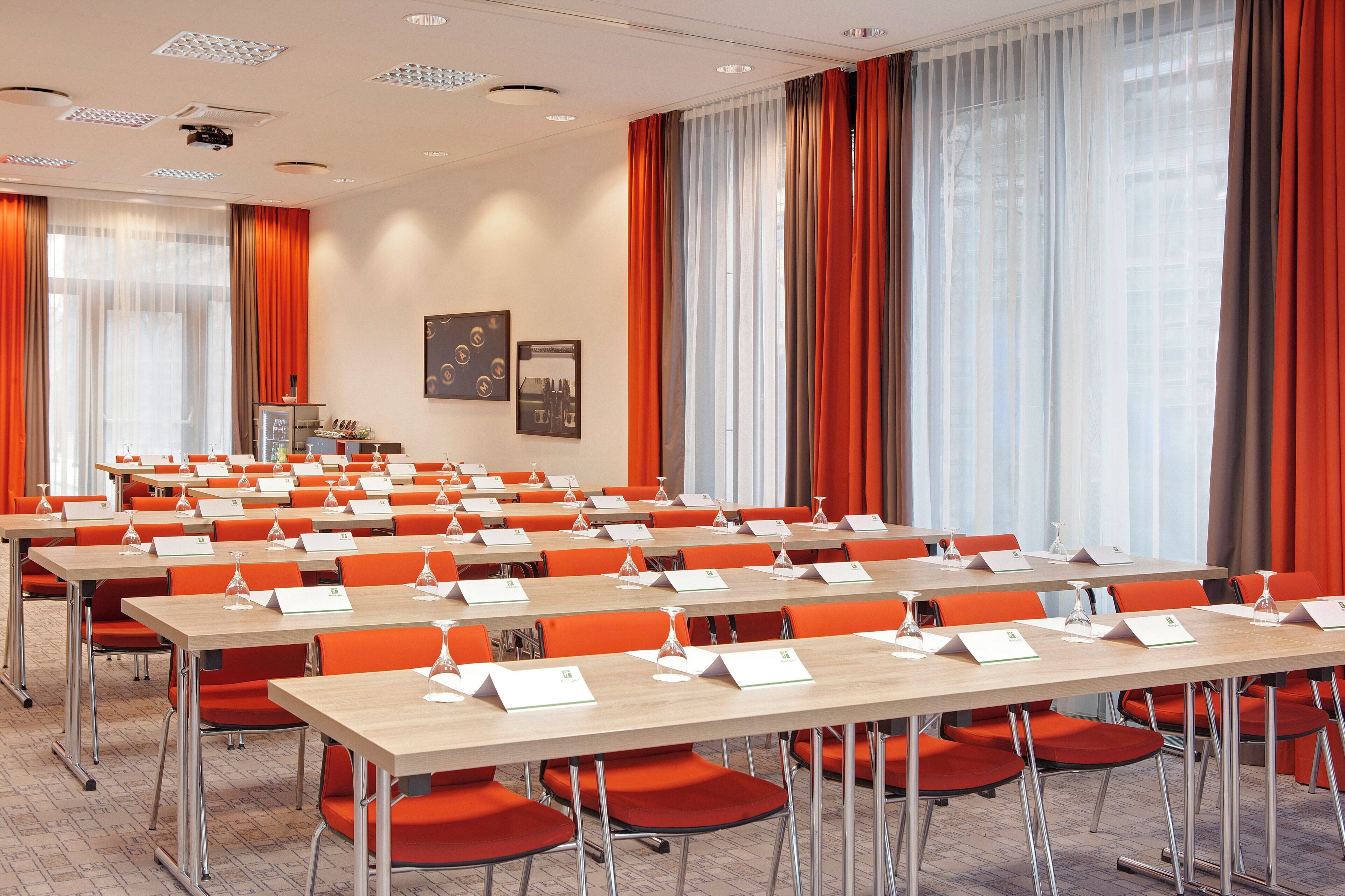 Ett konferensrum med flera bord och stolar, namnskyltar och en projektorduk.