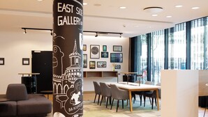 A modern interior with a dining area, a sofa, and a pillar with artwork. - Holiday Inn Berlin - City East Side by IHG (Berlin)