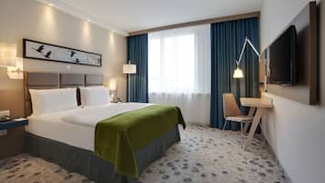 Ein Hotelzimmer mit einem großen Bett, einem Schreibtisch, einem Stuhl, einem Fernseher und einem Fenster mit Vorhängen.