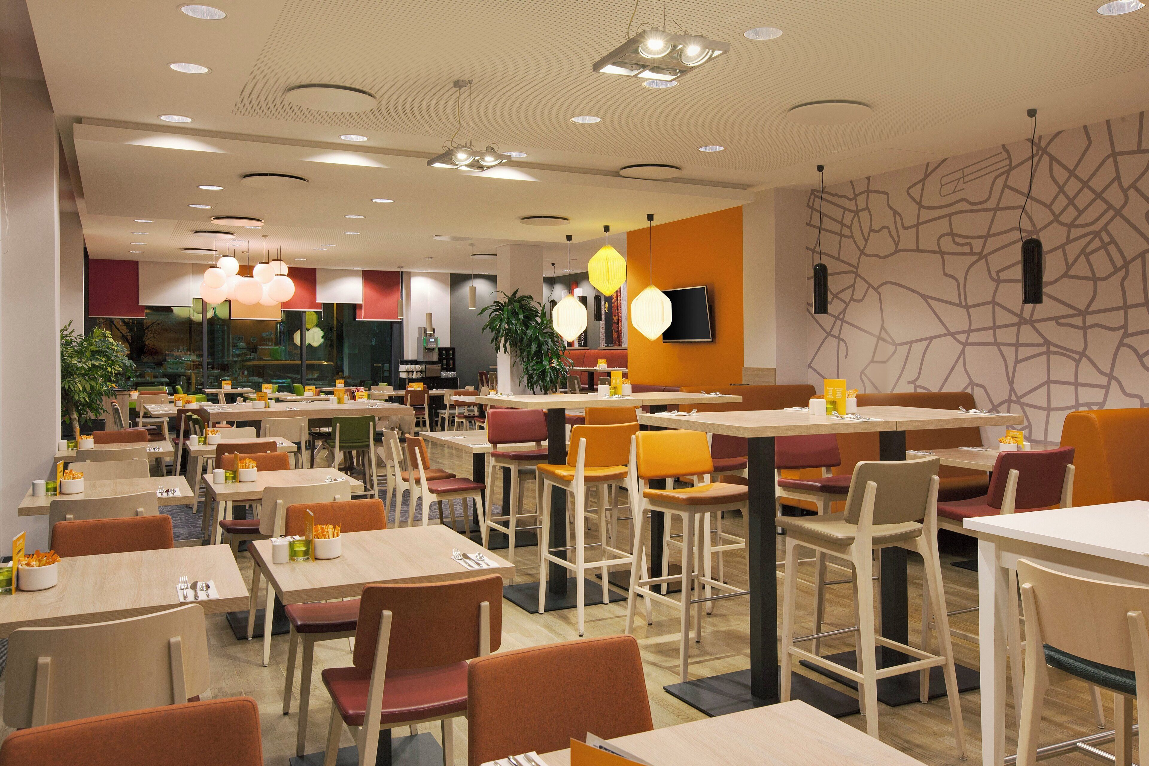 Ein modernes Restaurant-Interieur mit mehreren Tischen und Stühlen, einem an der Wand montierten Flachbildfernseher und einer Wand mit einem Kartenmuster.
