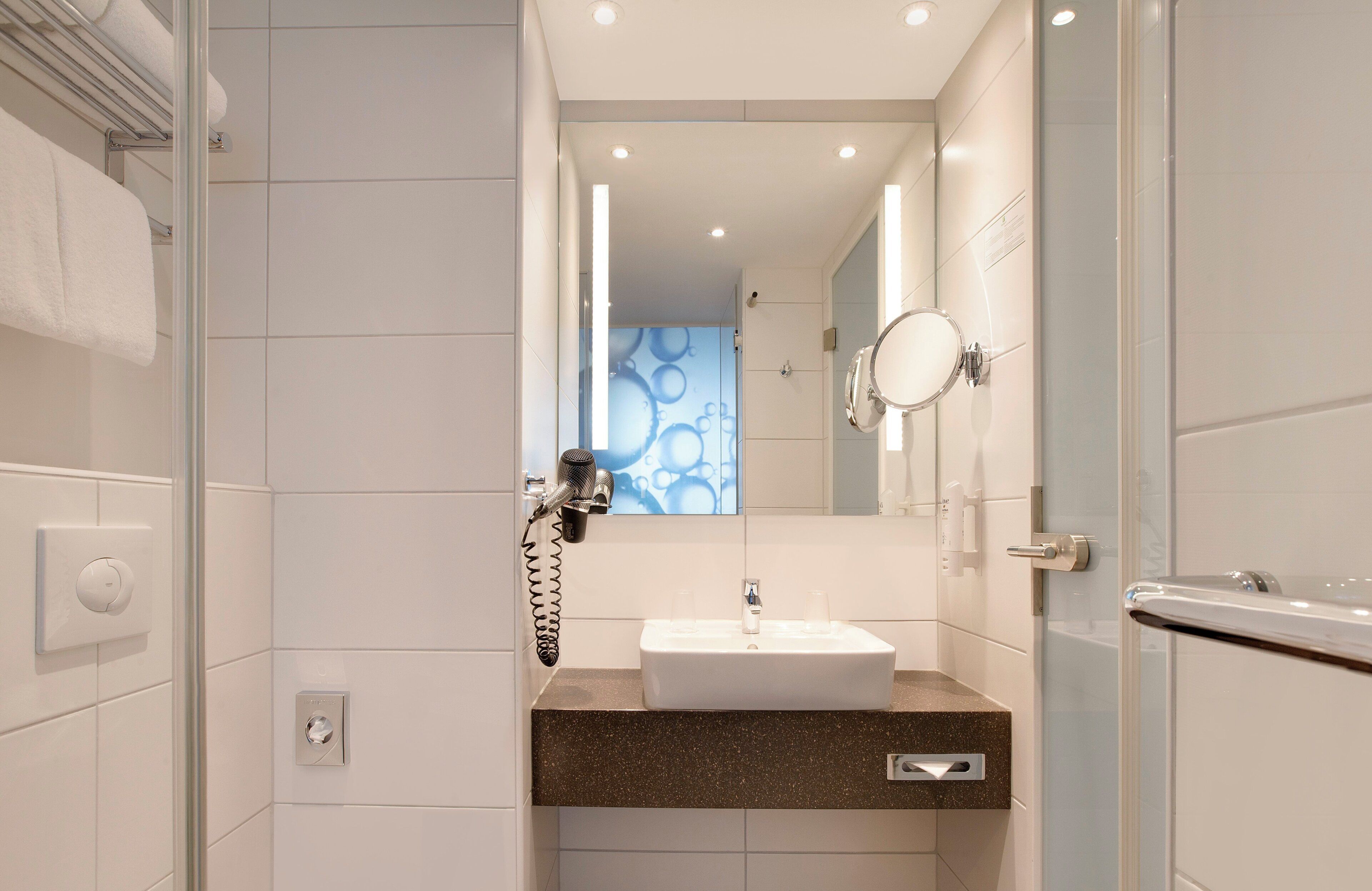 A modern bathroom with a glass shower enclosure, a white sink with a granite countertop, and a mirror with a round frame.