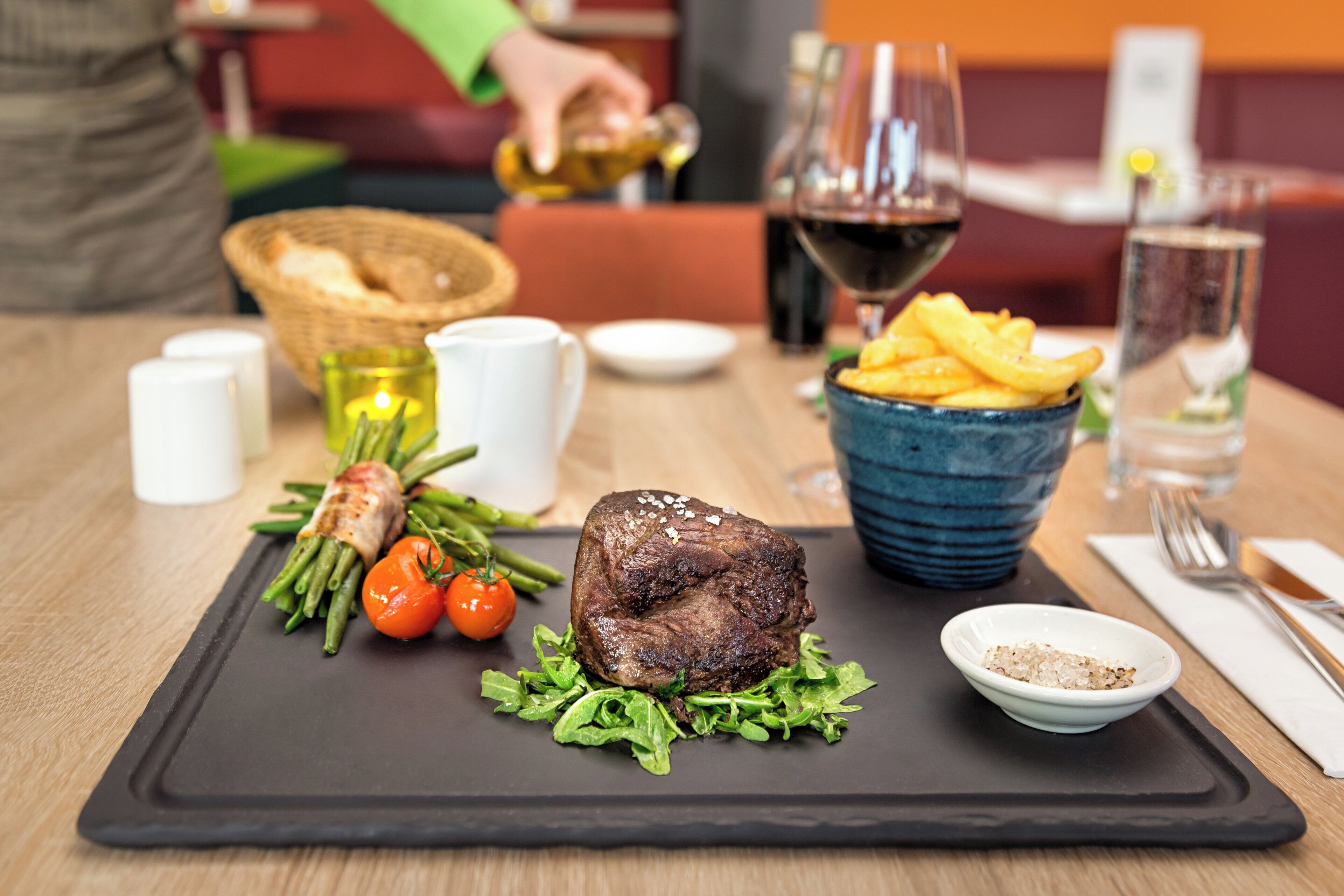 A dining table with a steak, green vegetables, and a bowl of fries.