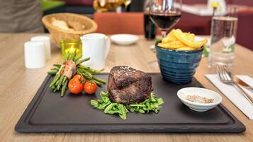 A dining table with a steak, green vegetables, and a bowl of fries.