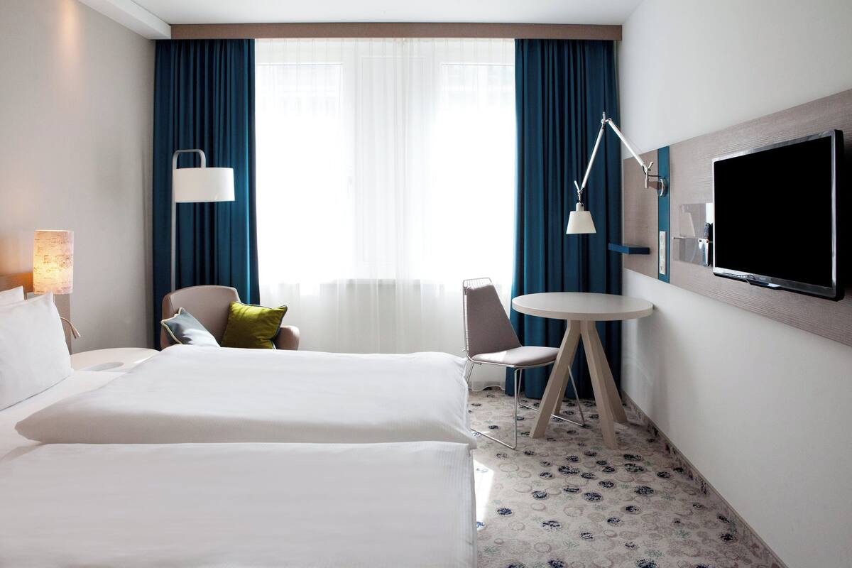 Habitación de hotel con dos camas, un escritorio, una silla, un televisor y una lámpara.