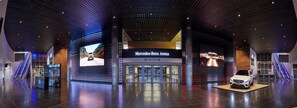 A modern indoor space with a Mercedes-Benz Arena sign, escalators, and a display of a white car. - Holiday Inn Berlin - City East Side by IHG (Berlin)