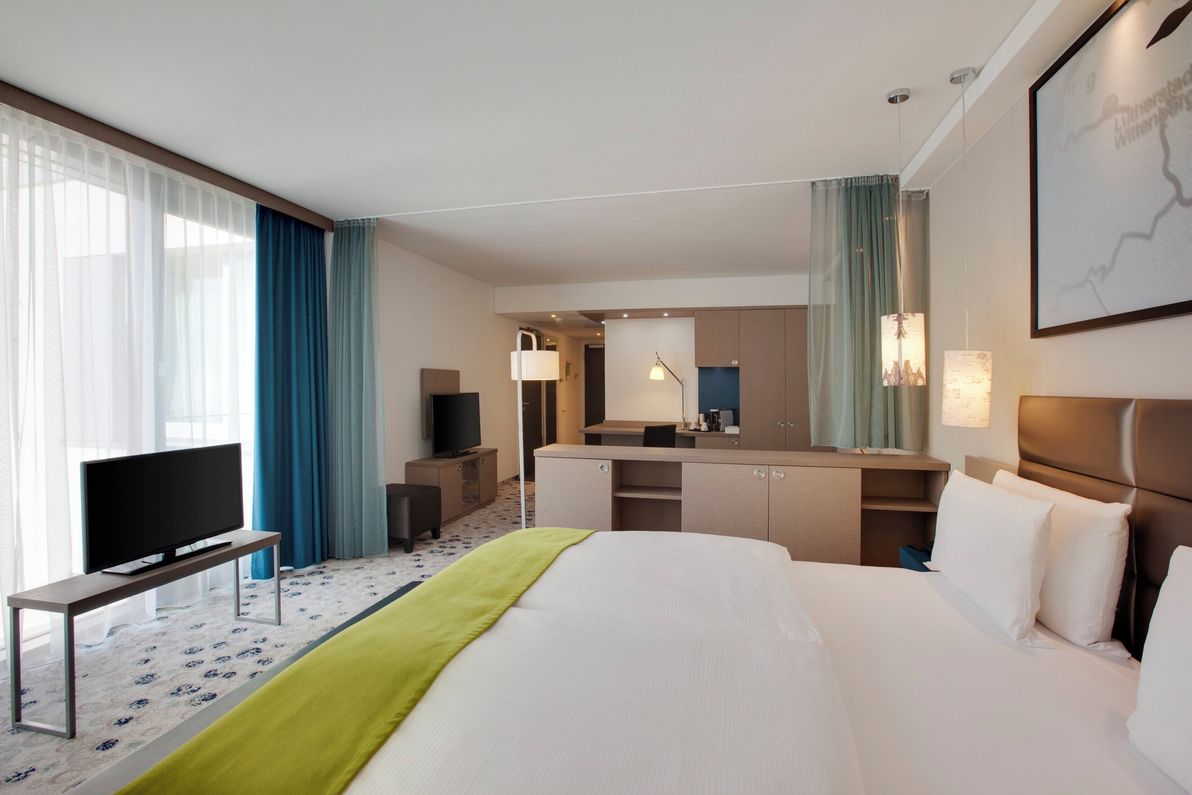 A hotel room with a bed, a desk, a television, a mirror, and a window with curtains.